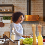 A Black women in a kitchen with brick walls making a salad showing what I eat during my period